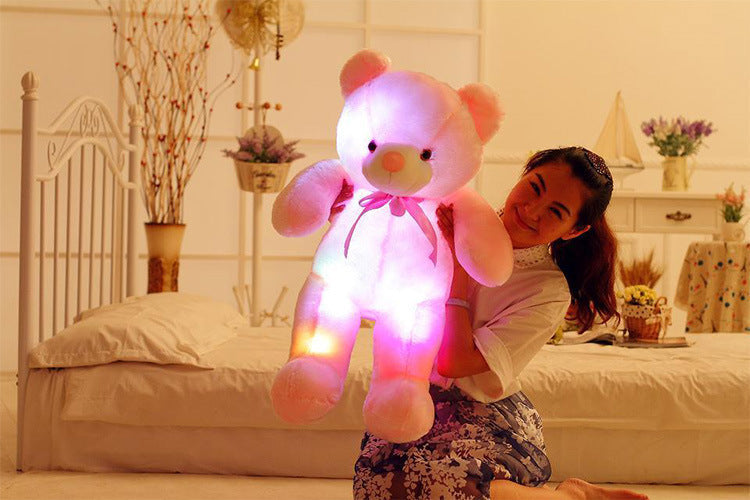 Girl holding a large, glowing pink teddy bear in a cozy room, showcasing soft toys collection for imaginative play.