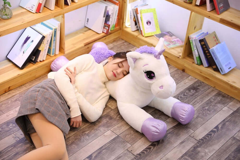 A child peacefully sleeping with a plush unicorn pillow soft toy in a cozy reading nook, perfect for toddlers and children.